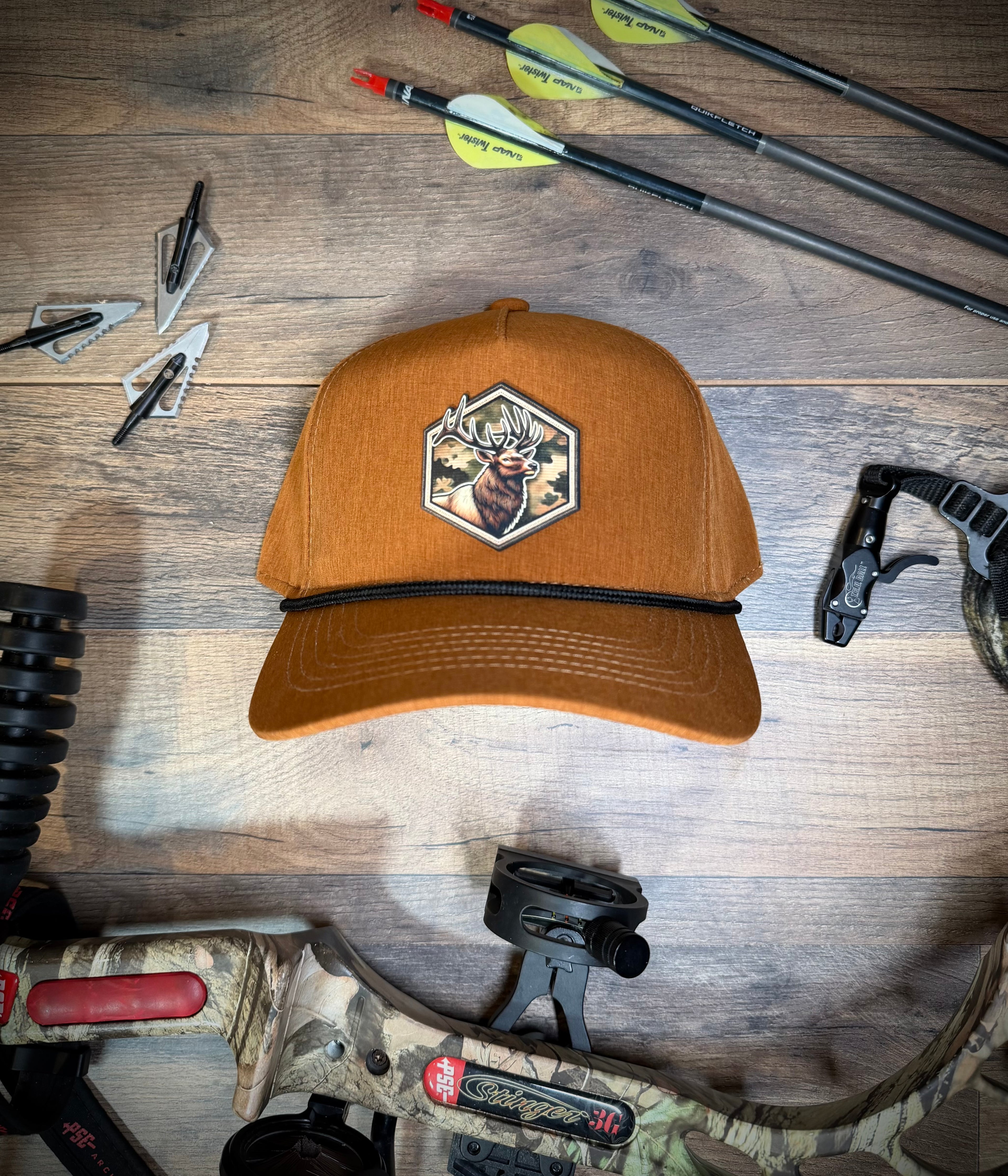 Brown cap with hunting design on a wooden surface with archery equipment.