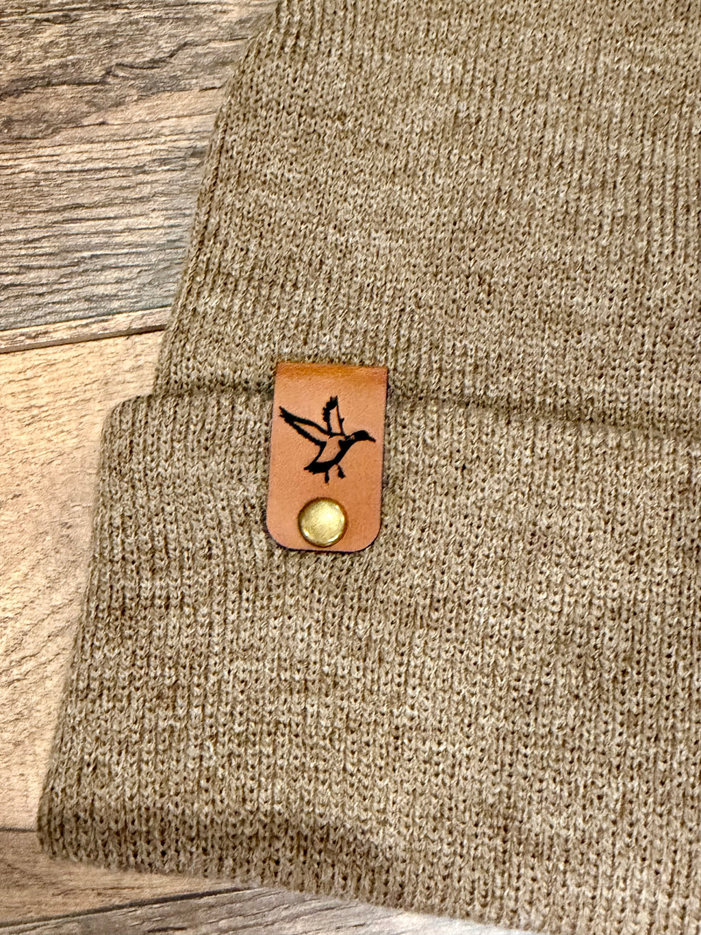 Brown knit sweater with a leather patch featuring a bird design on a wooden surface