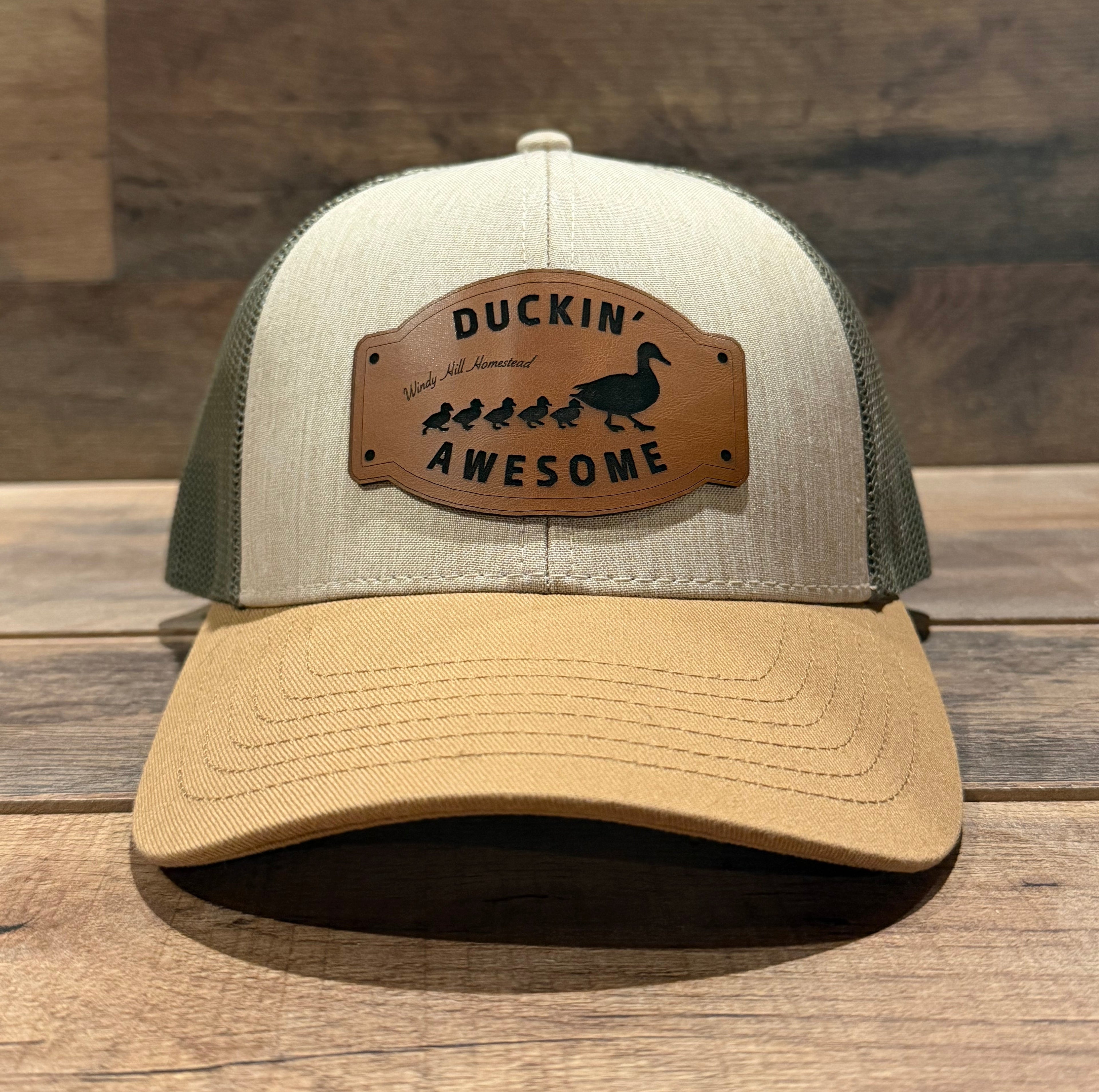 Two hats, one beige and one green, on a wooden surface with a 'Duckin' Awesome' patch.