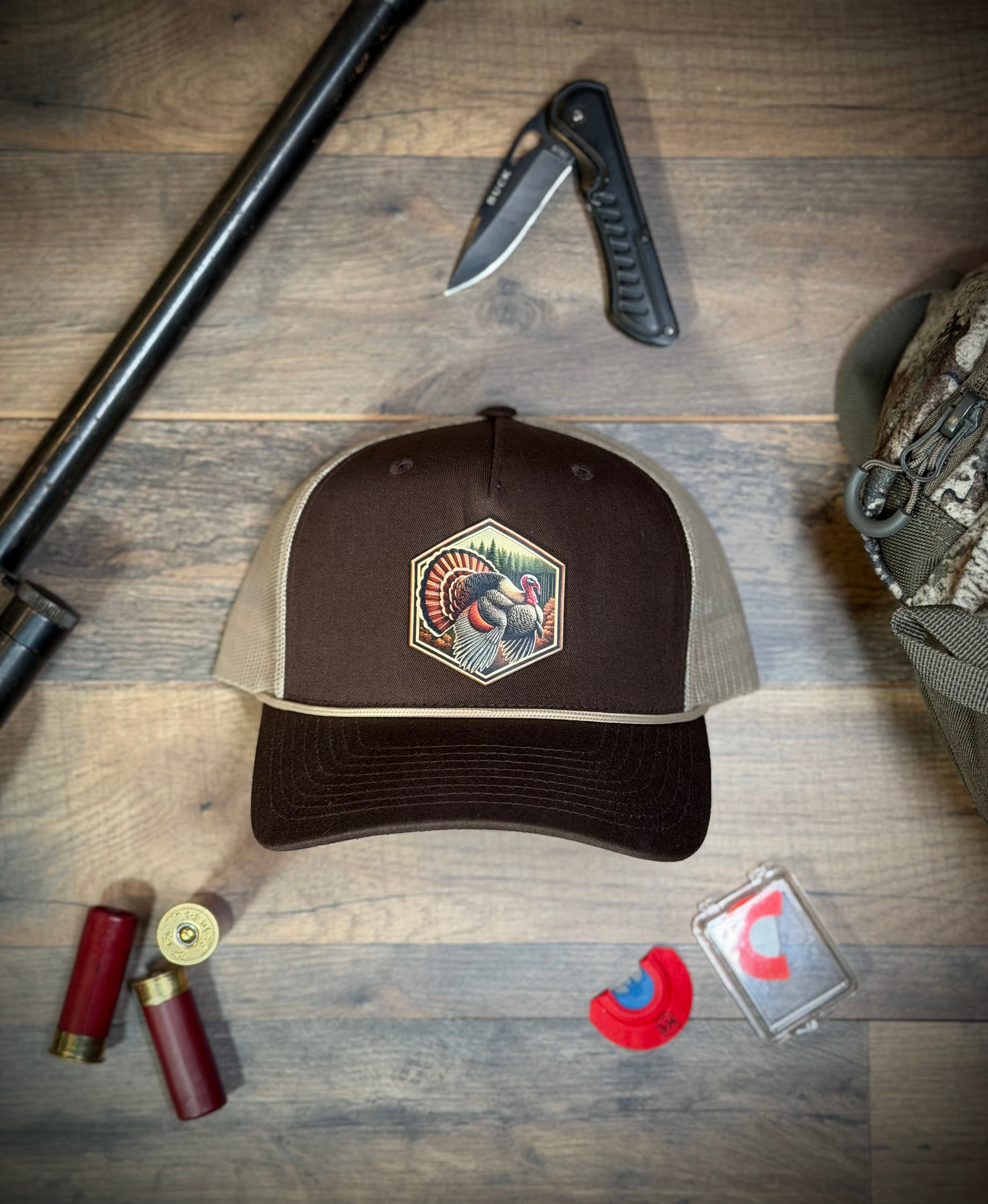 Brown and beige cap with a logo on a wooden surface with hunting equipment.