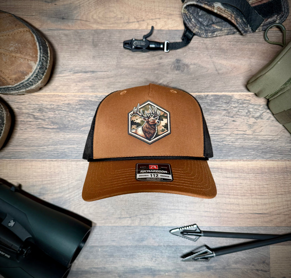Brown and black cap with hunting design on a wooden surface with hunting gear.