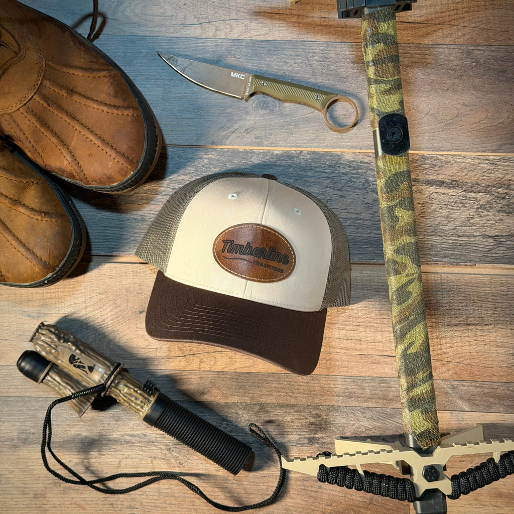 Hunting gear including a knife, binoculars, boots, and a cap on a wooden surface.
