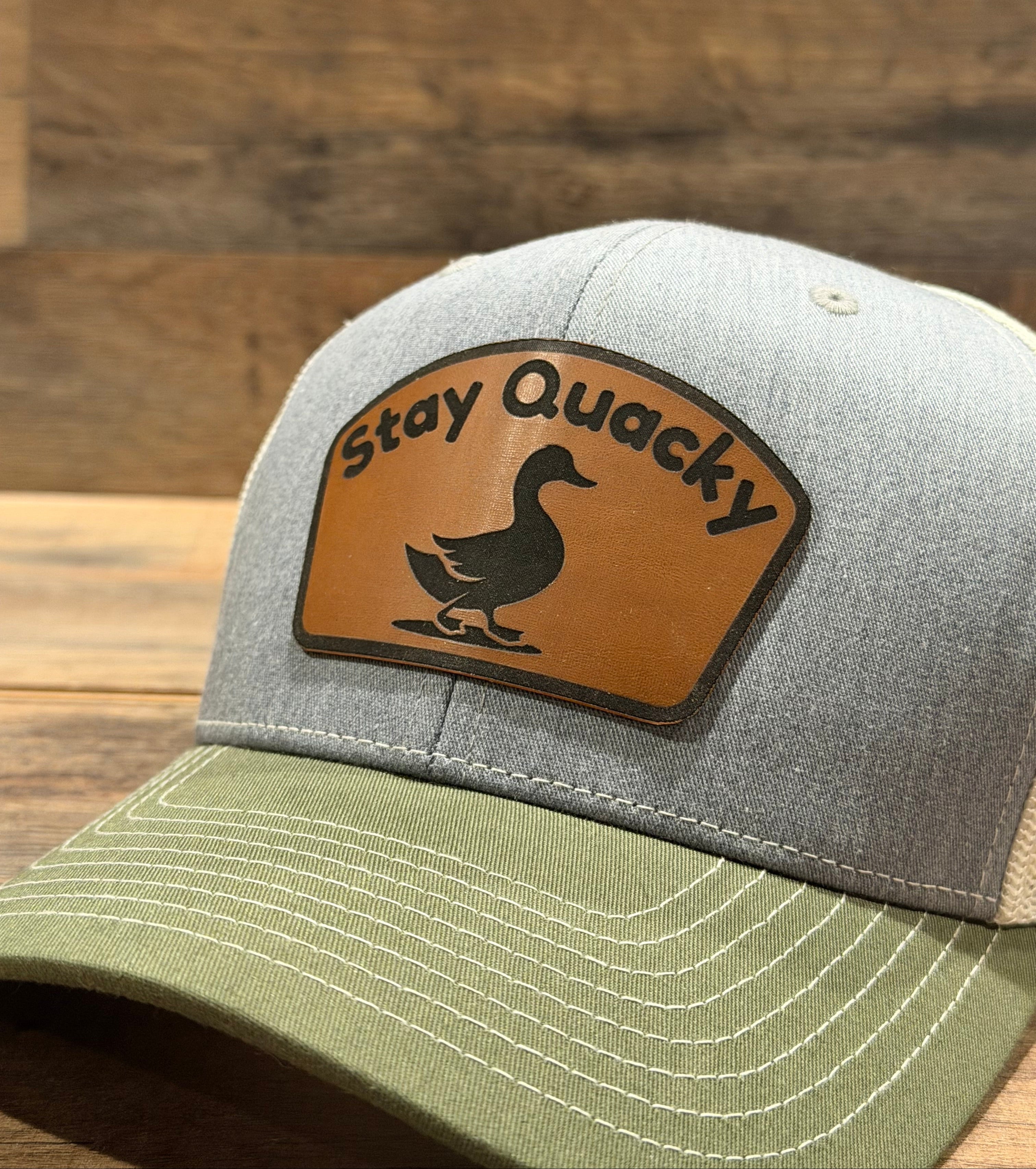 Trucker hat with a 'Stay Quacky' patch on a wooden surface