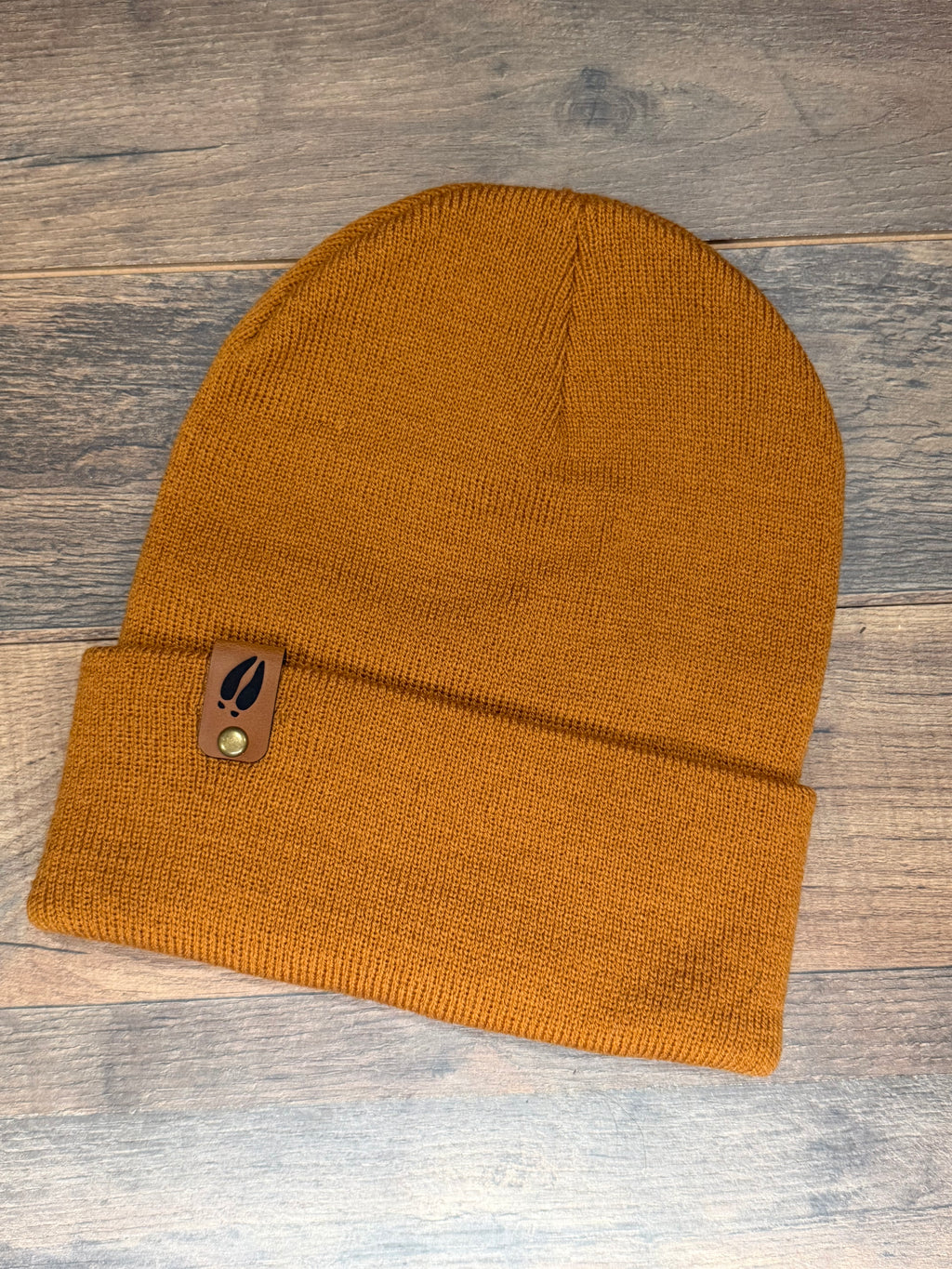 Mustard yellow knit beanie with a brand tag on a wooden surface