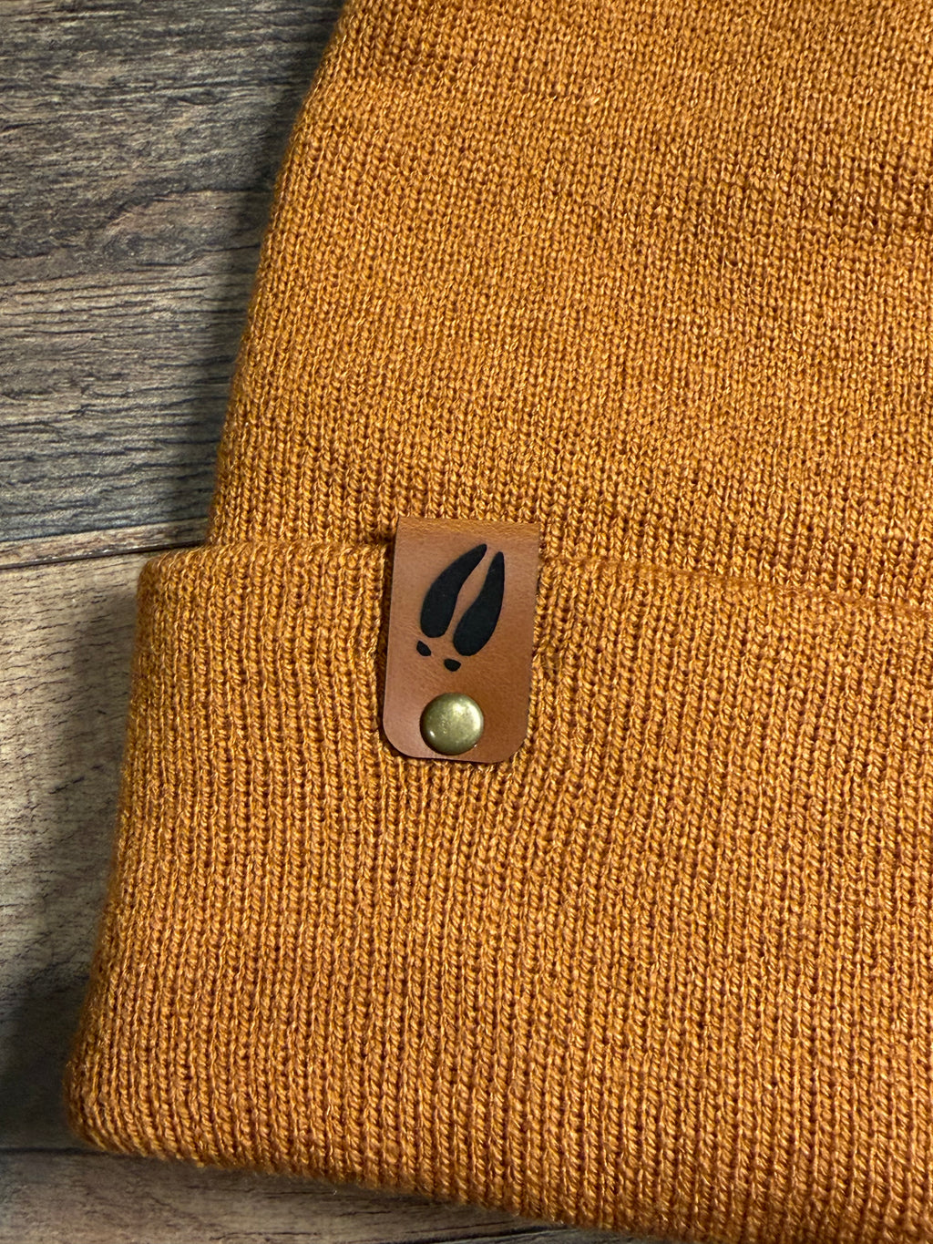 Brown textured fabric with a leather patch featuring a leaf design on a wooden surface