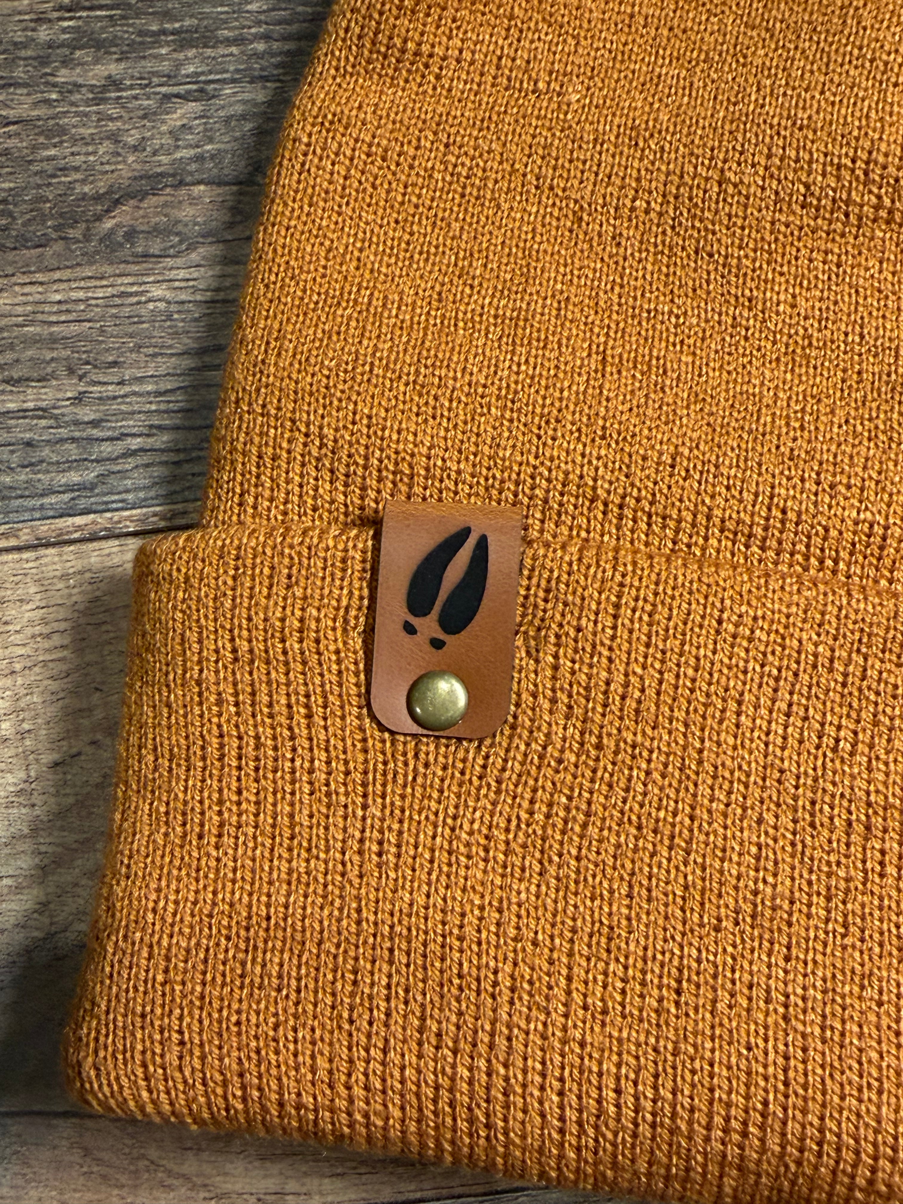 Brown textured fabric with a leather patch featuring a leaf design on a wooden surface